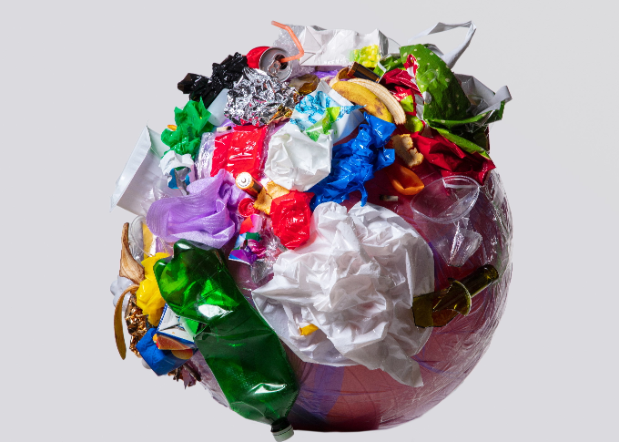 A spherical object covered in various types of trash, including plastic bottles, paper, and food waste