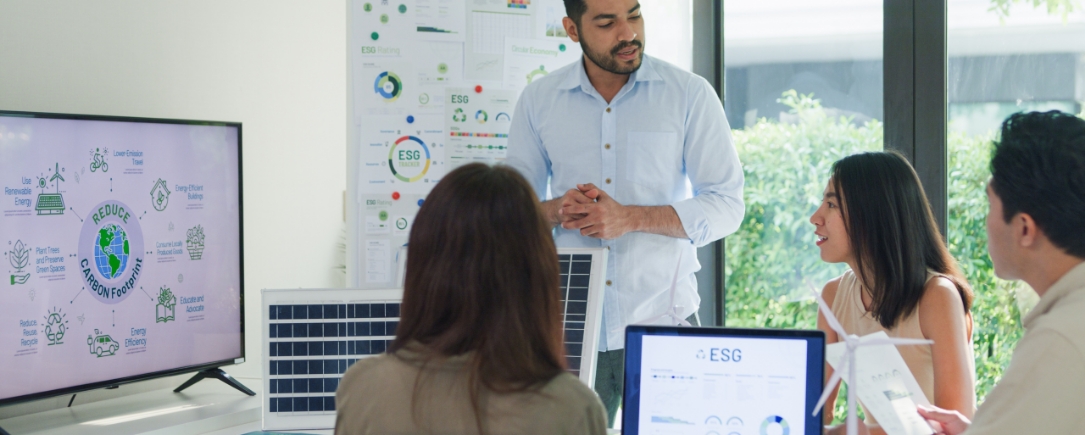 A group of individuals in a meeting room with digital screens displaying graphs and charts, discussing the Inrate ESG screening tool.